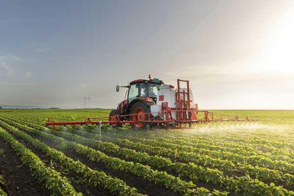 Photo of agricultural equipment on farm spraying field of crops.