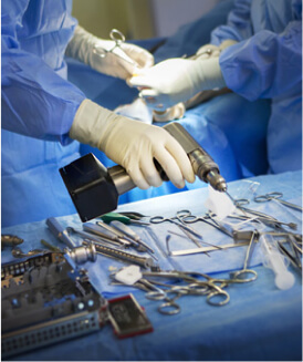 Hands of two doctors over a row of medical tools, one holding a forceps, the other holding a surgical drill