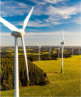 Windmills in windfarm rise above fields and trees 