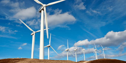 Looking up at Wind Turbines on a hill against a sunny sky