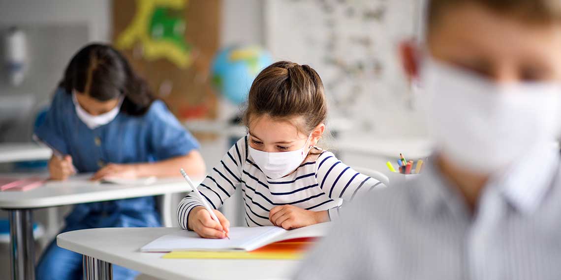 Photo of three masked children at their desks in school.