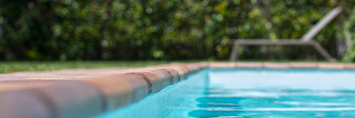 Photo of side of pool with tan bricks and chair in the back. Header for  quieter pool pump motor story.