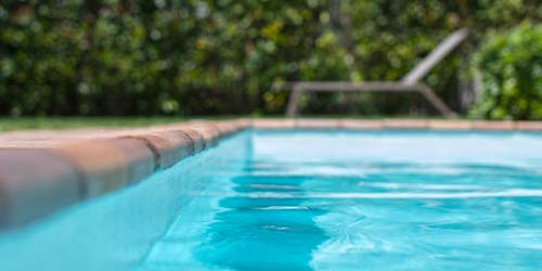 Photo of outdoor pool with tan bricks and a chair in the background. 