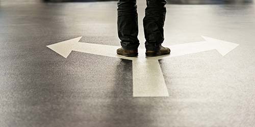 Photo of person's feet standing on two directional arrows.