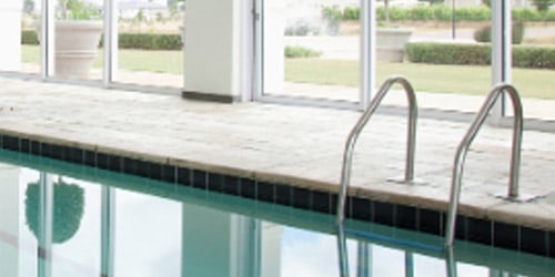 Photo of swimming pool with windows reflected in the water and a ladder.