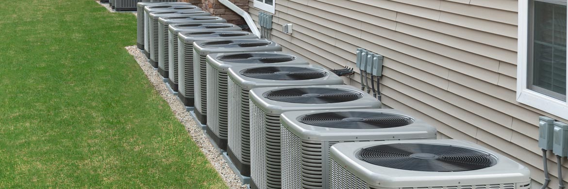Row of outdoor air conditioner units behind multifamily residential dwelling.