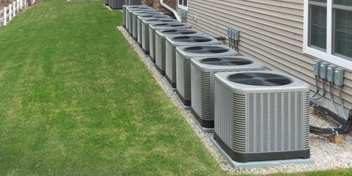 Row of outdoor air conditioner units behind multifamily residential dwelling.