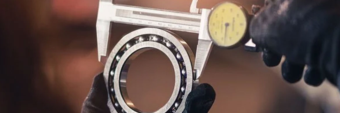 Gloved hands holding tool measuring clearance of a ball bearing.