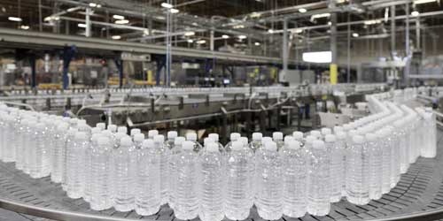 Line of filled water bottles on conveyor machine.