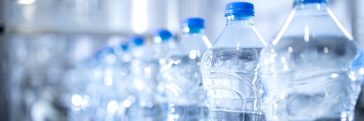 Row of clear filled bottles with blue caps on production line.