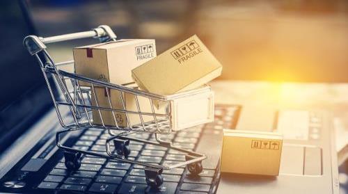Image of Miniature shopping cart filled with packages sitting on a laptop keyboard
